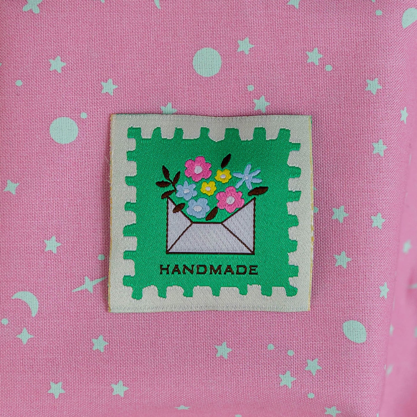 Pink fabric with green star pattern and a 'Handmade' label featuring flowers and an envelope.