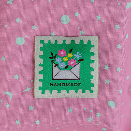 Pink fabric with green star pattern and a 'Handmade' label featuring flowers and an envelope.